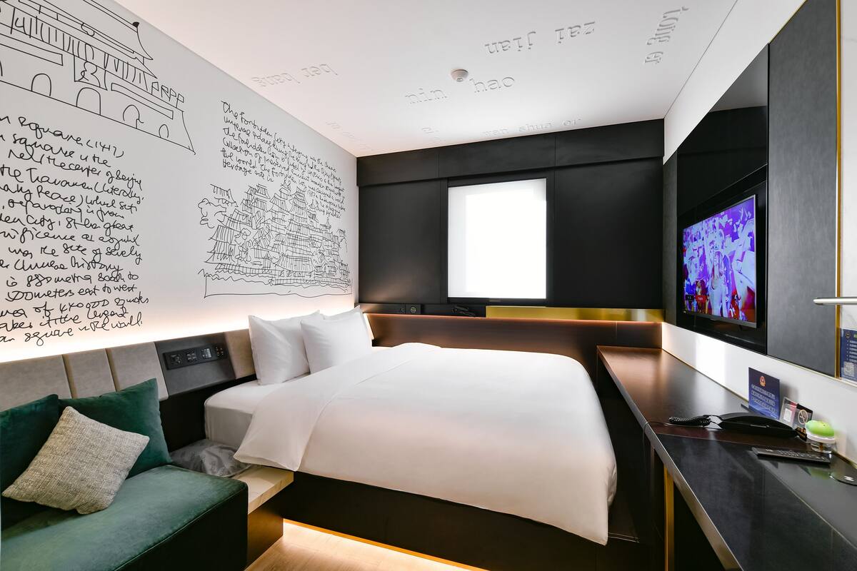 A modern hotel room with a large bed, a desk, and a television.