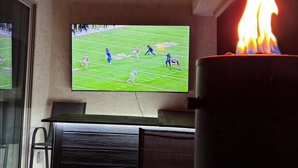 A room with a television displaying a football game, a ceiling fan, and a lit candle. - Luxury Glendale Stay with Pool & Theater Room by Cardinals Stadium (Glendale)