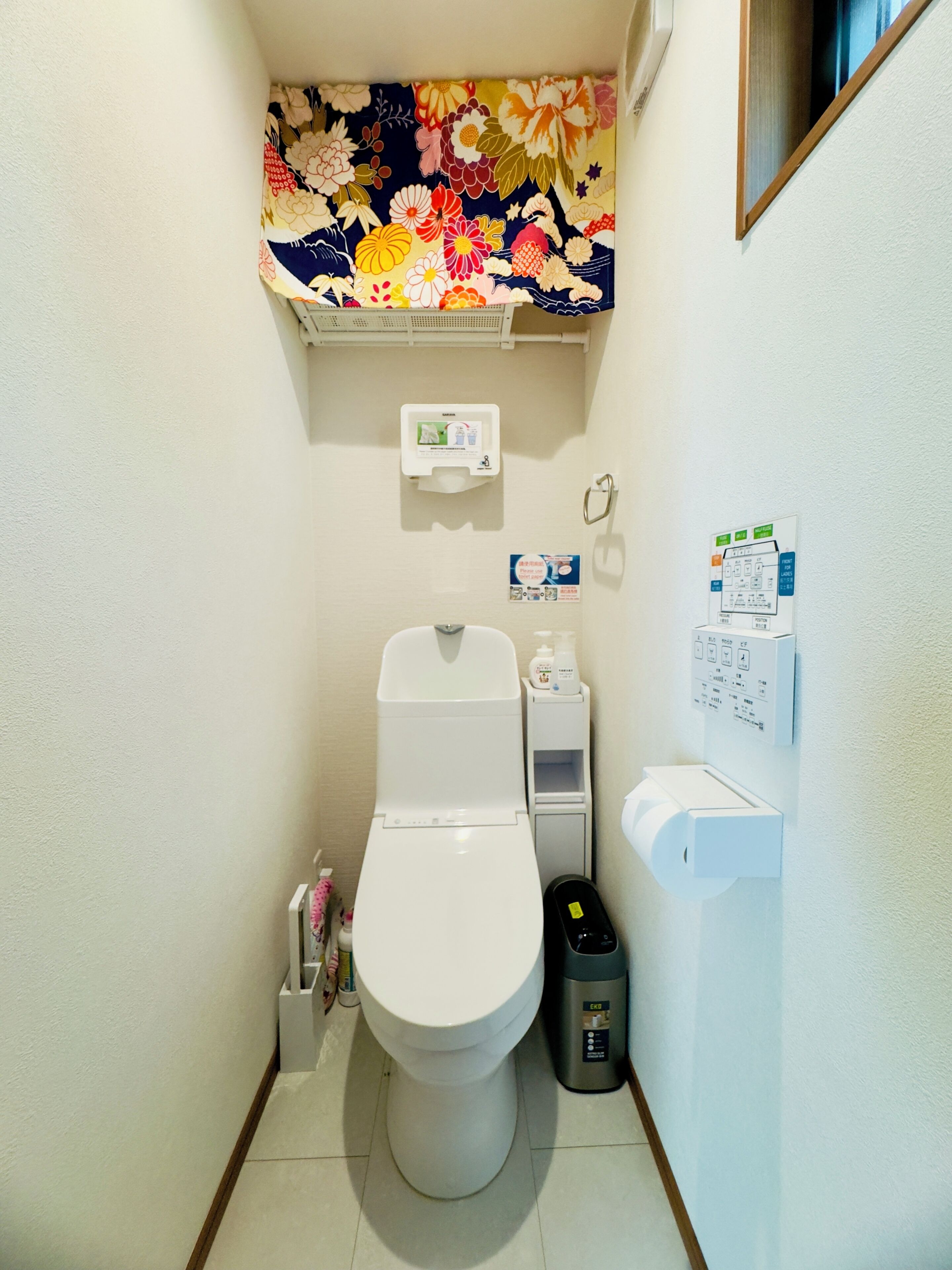 A small, compact bathroom with a toilet, a hand dryer, a paper towel dispenser, and a trash can.