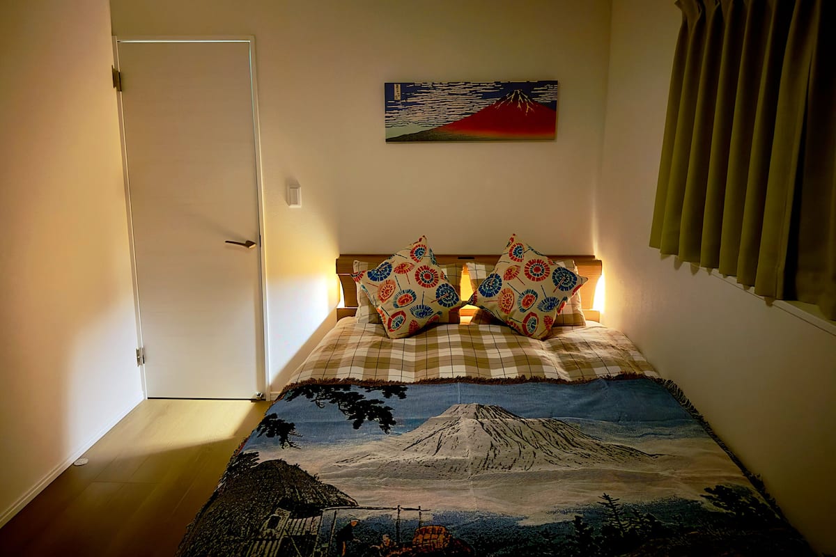 A bedroom with a bed, a door, a wall-mounted painting, and a window with curtains.