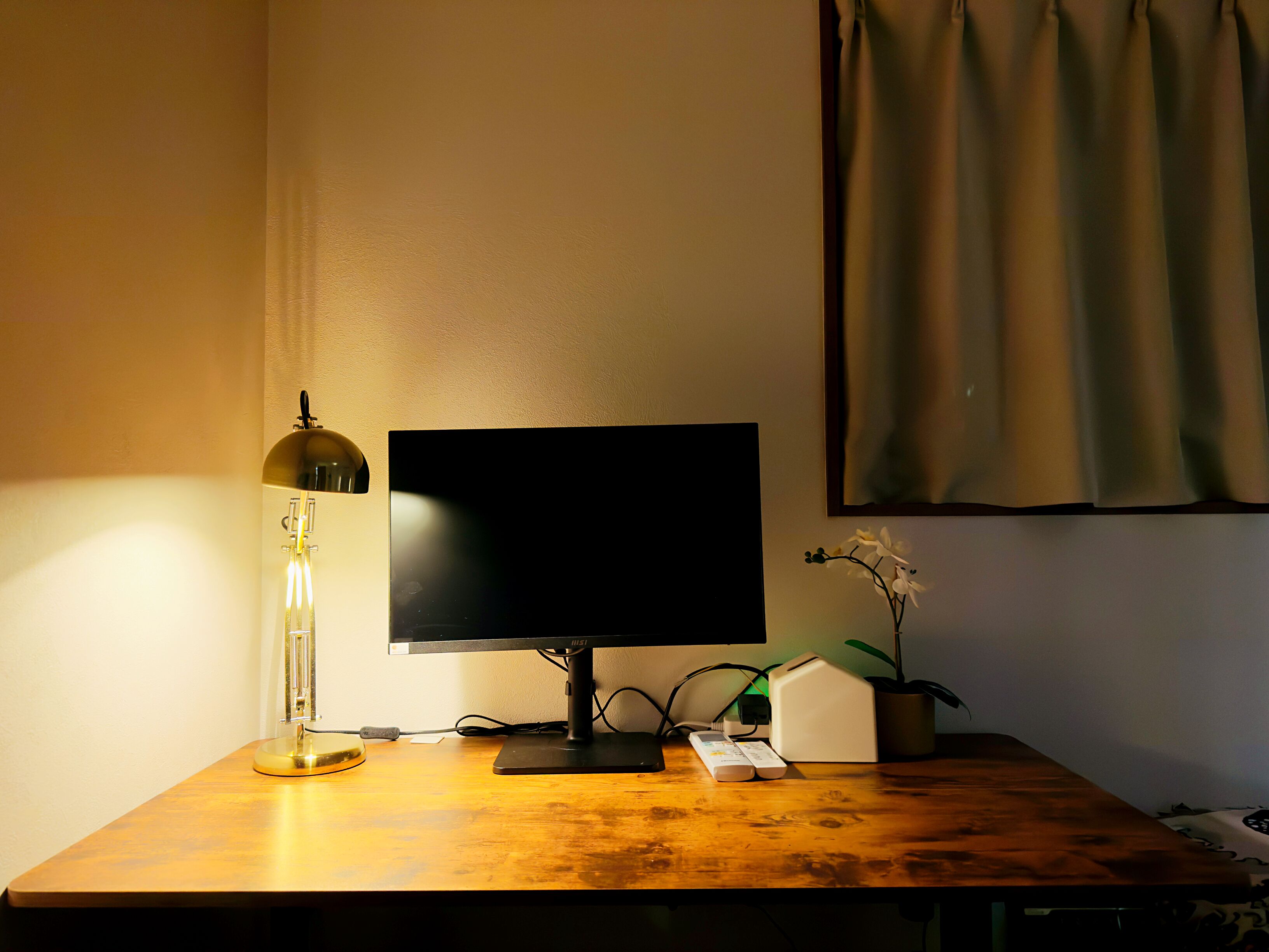 Een bureau met een computer, een lamp, een plant en een stekkerdoos.