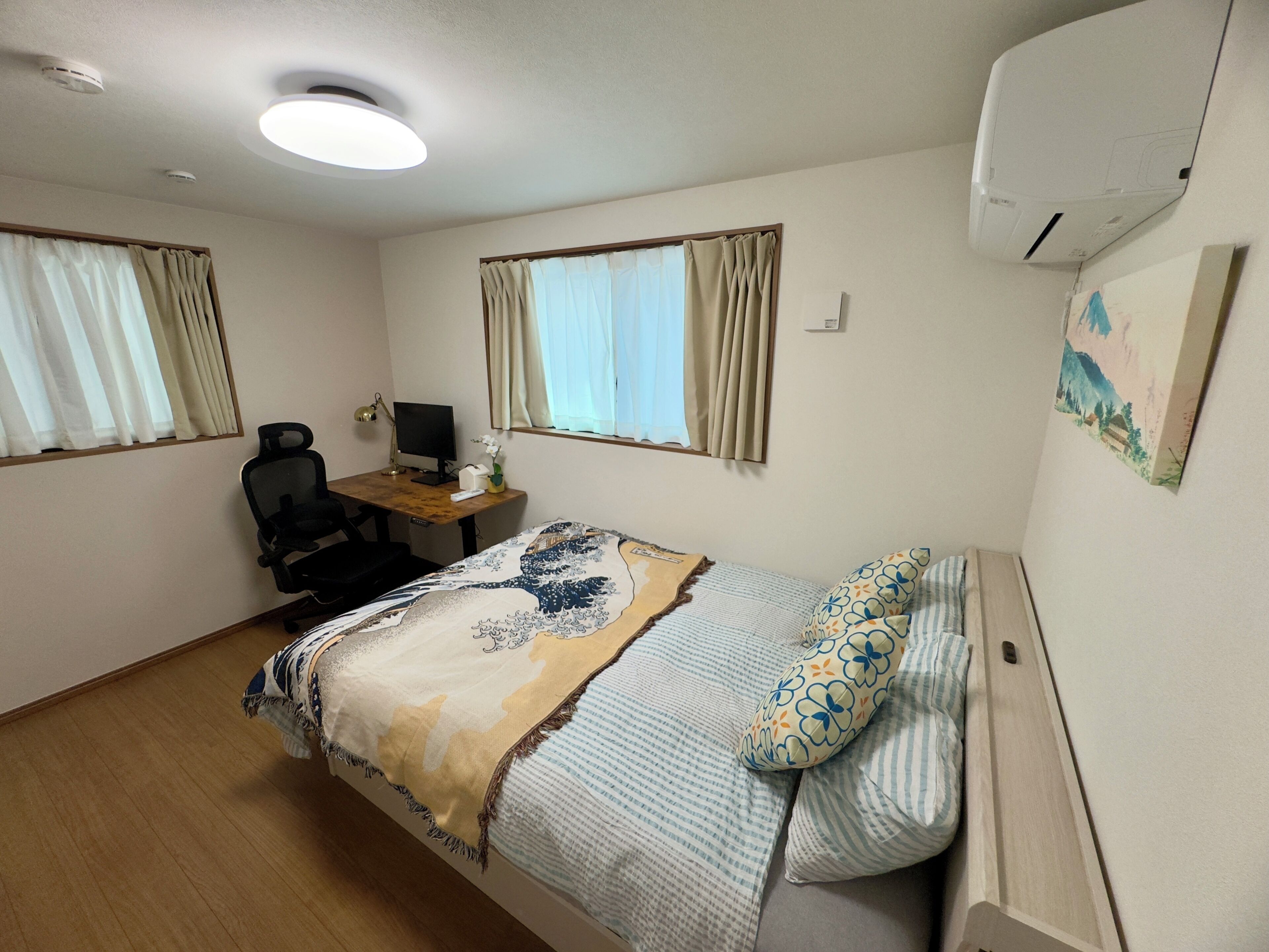 A bedroom with a bed, a desk with a computer, a chair, and an air conditioner.