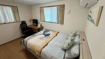 A bedroom with a bed, a desk with a computer, a chair, and an air conditioner.