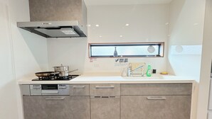 A modern kitchen with a gas stove, dishwasher, and a window above the sink. - Hao Bros.Home Gemini (Tokyo)