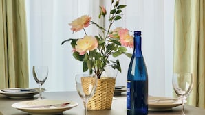 A dining table with plates, cutlery, a vase with flowers, a blue bottle, and a woven basket. - Hao Bros.Home Gemini (Tokyo)