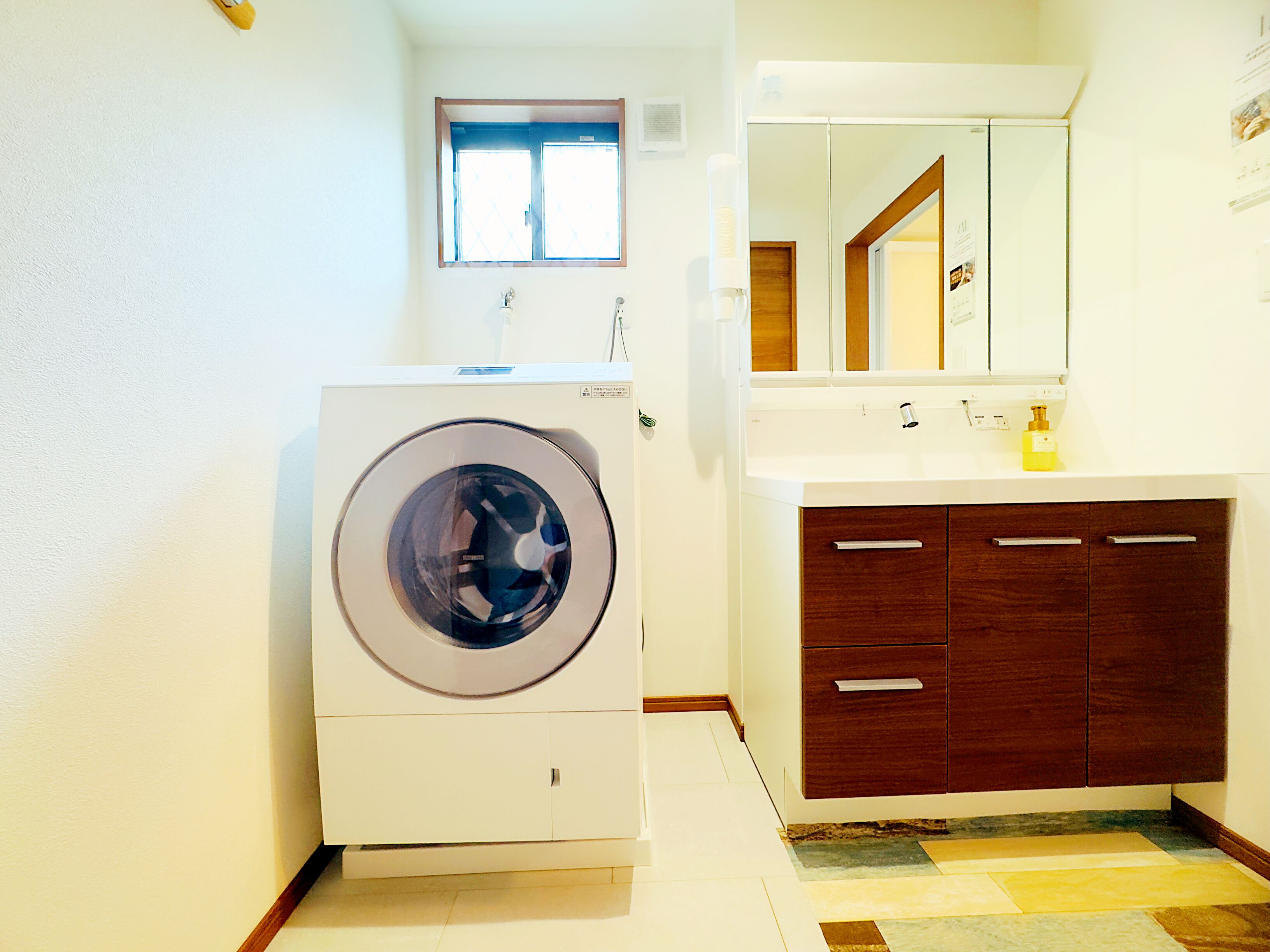 A compact laundry room with a front-loading washing machine, a sink with a mirror above it, and a wooden cabinet below.
