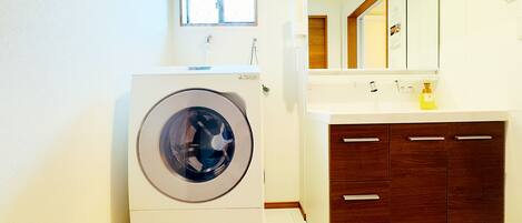 A compact laundry room with a front-loading washing machine, a sink with a mirror above it, and a wooden cabinet below.