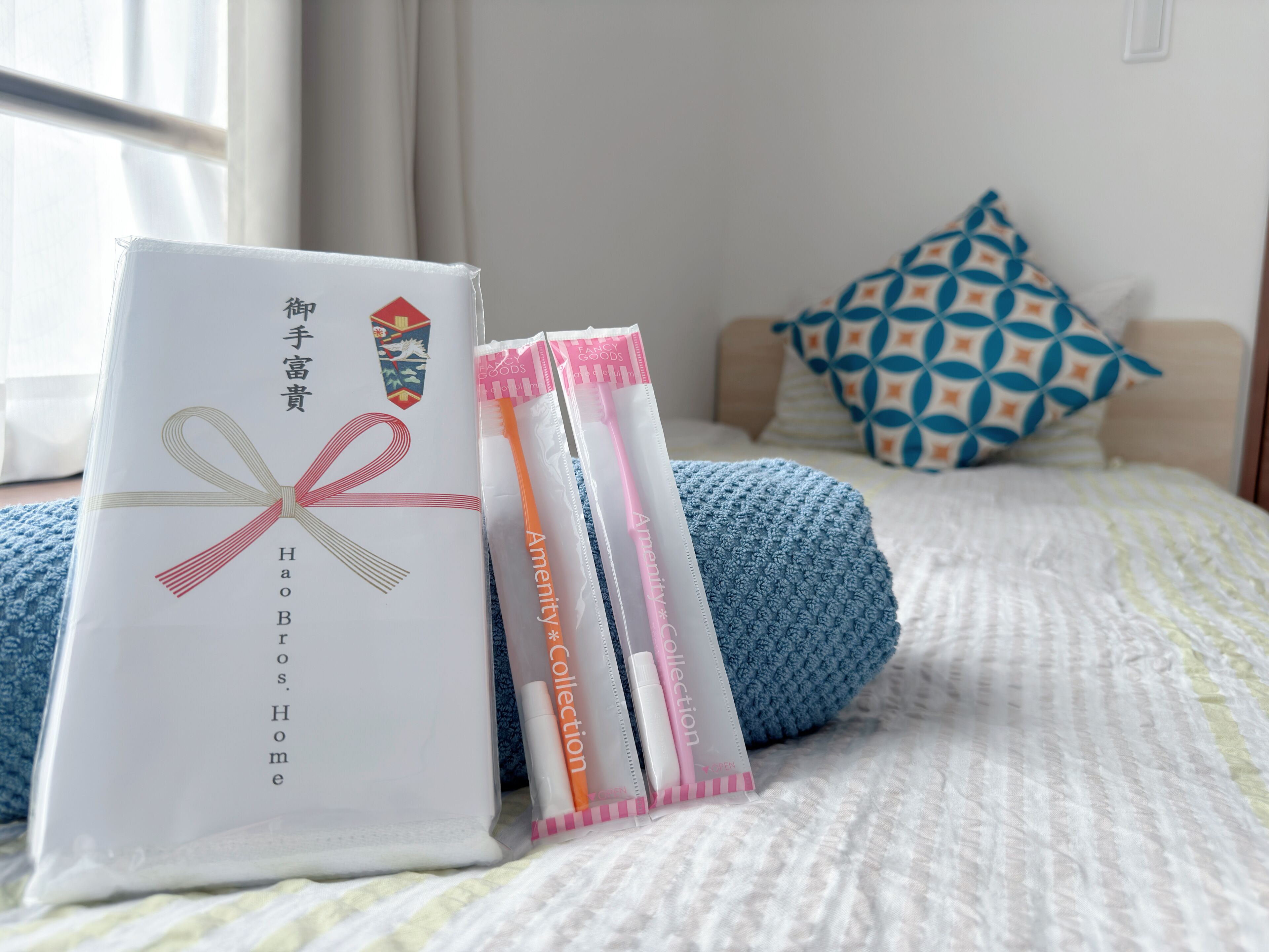 A neatly arranged bed with a blue blanket, pillows, and a white package with a ribbon.
