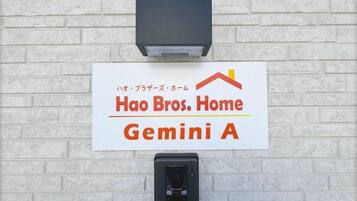 A sign for 'Hao Bros. Home Gemini A' on a white brick wall with a black electrical box below it.