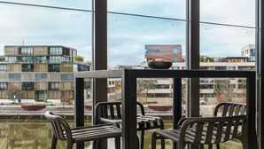 Blick aus einem Fenster mit Tisch und Stühlen auf moderne Gebäude und ein Gewässer.