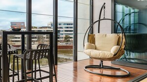 Ein modernes Zimmer mit Hängekorbschaukel, Holztisch und großen Fenstern mit Blick auf Gebäude und ein Gewässer.