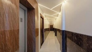 A long, narrow hallway with a marble floor and walls, leading to a door at the end. - Heaven Grand Ayodhya (Sohawal)