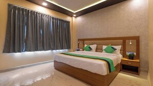A bedroom with a large bed, a nightstand, a window with curtains, and a wall-mounted light fixture. - Heaven Grand Ayodhya (Sohawal)