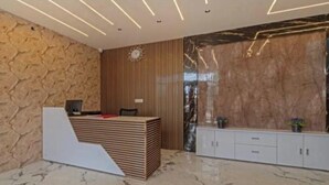 A reception area with a wooden reception desk, a clock, and a marble wall. - Heaven Grand Ayodhya (Sohawal)