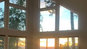 A room with large windows, a small table with flowers, and a view of trees and sky.