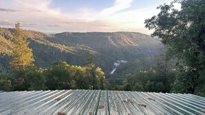 A view from a covered outdoor area with a metal roof, overlooking a forested valley and a river.