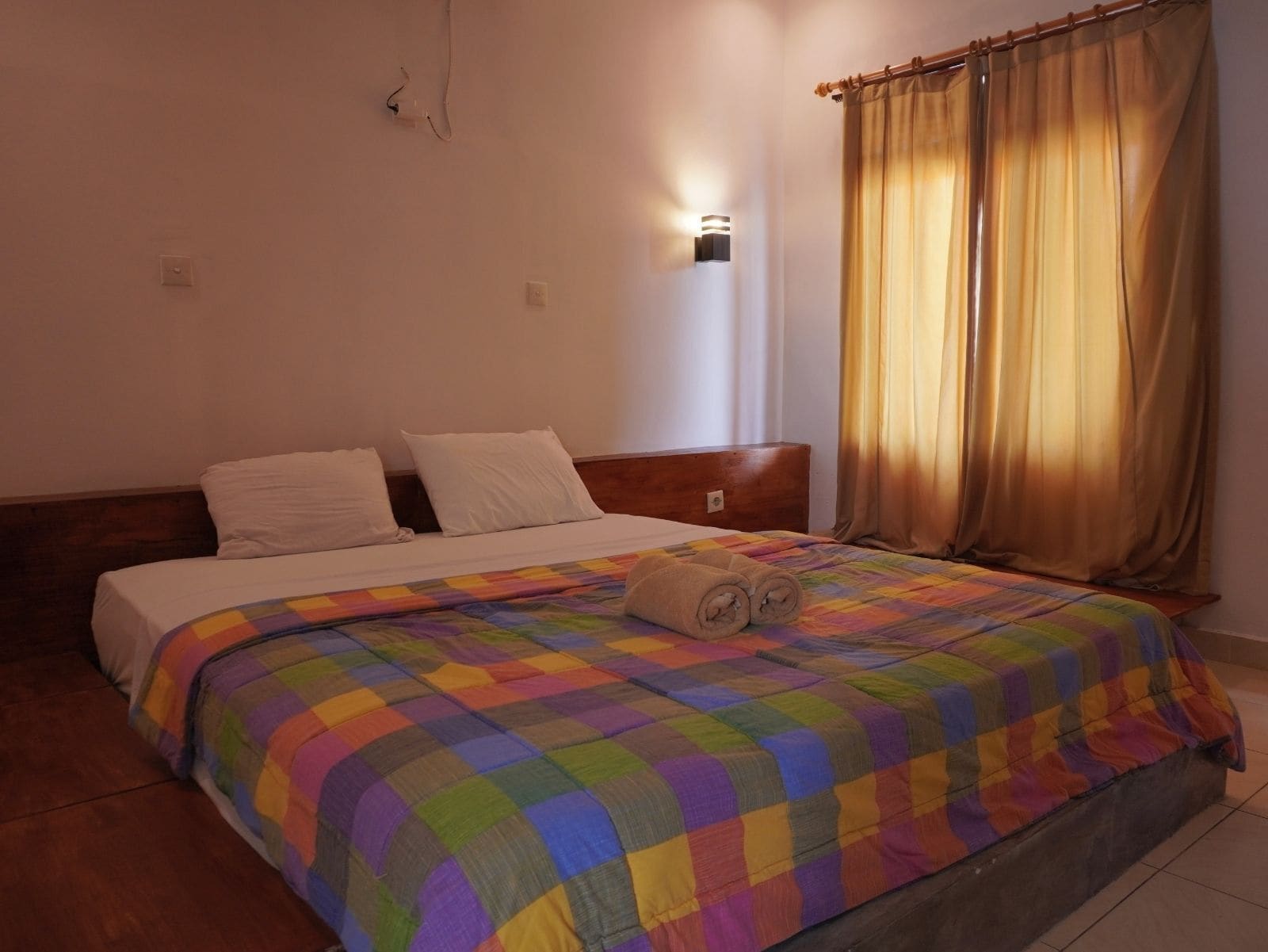 A bed with a colorful quilt, a wooden headboard, and a wall-mounted light fixture.