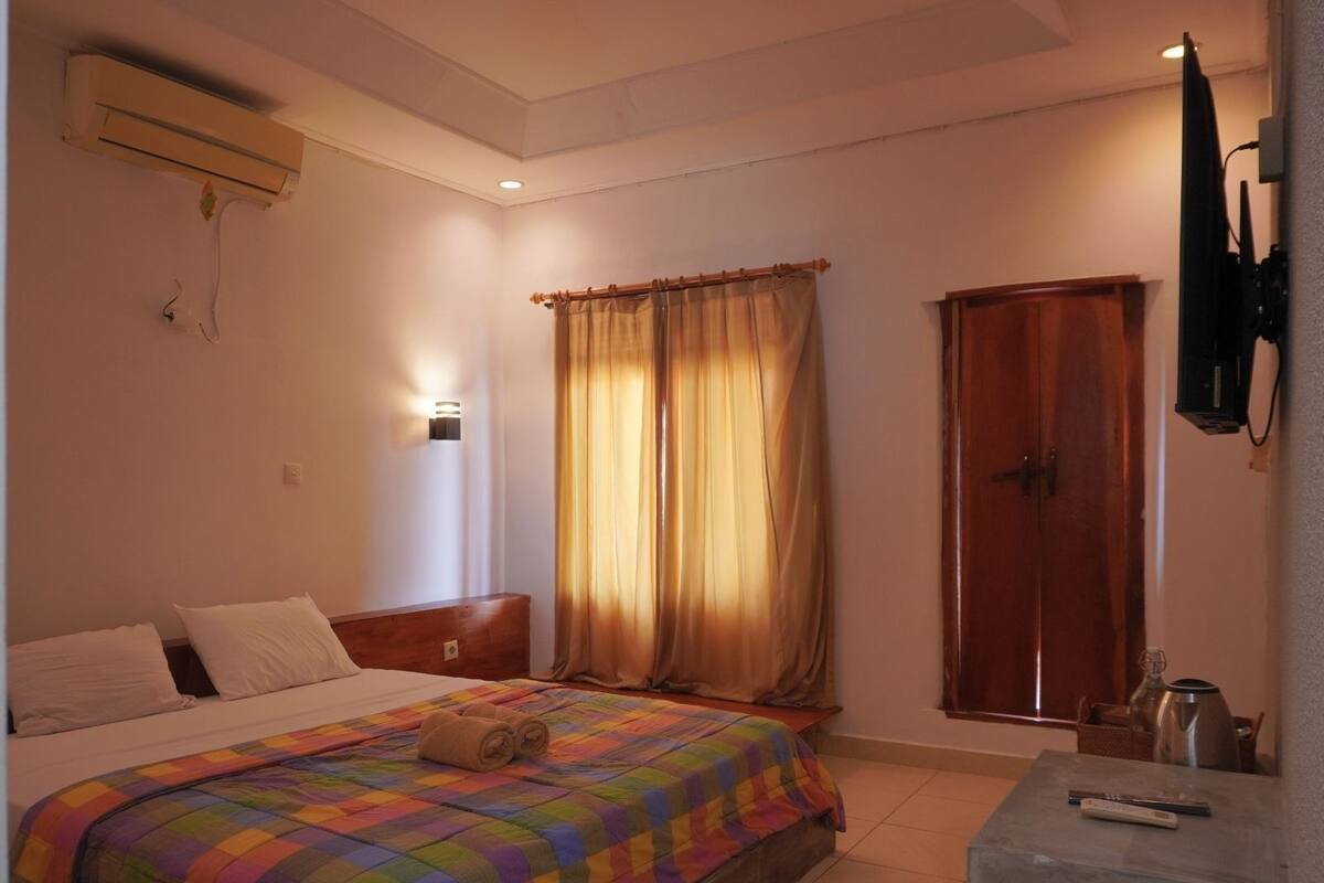 A bedroom with a bed, a nightstand, a TV, a wardrobe, and a window with curtains.
