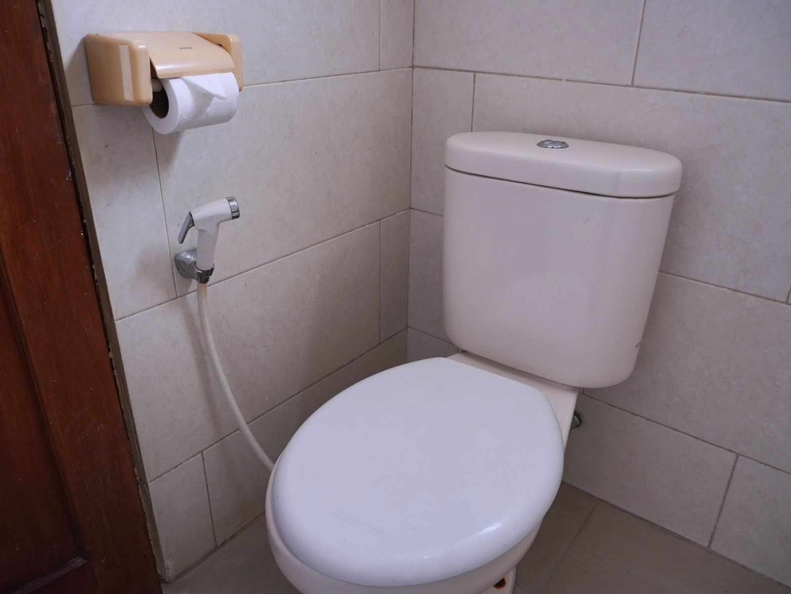Een standaard wit toilet met een papieren handdoekdispenser en een bedieningsknop.