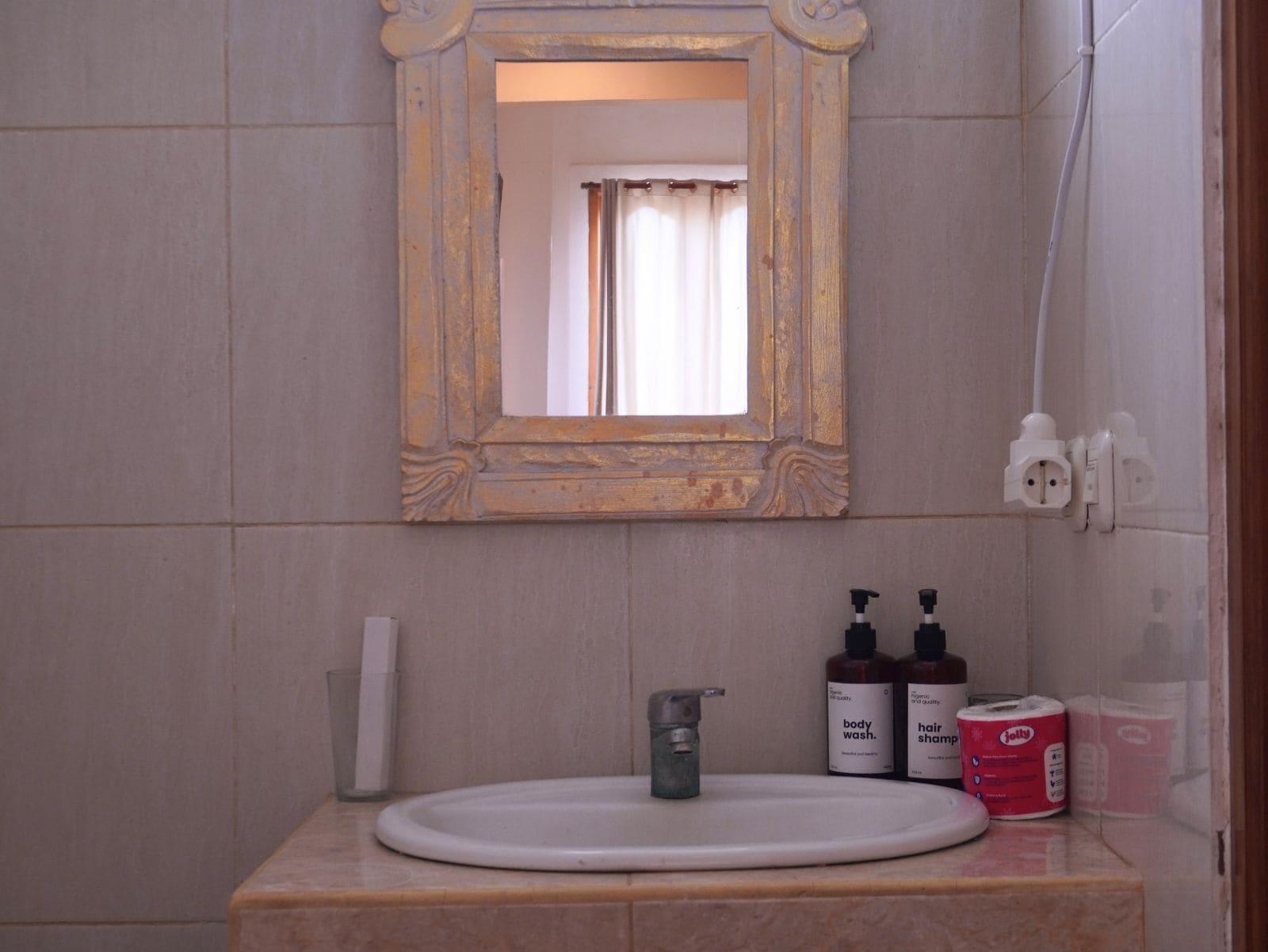 A bathroom with a white sink, a mirror with an ornate frame, and toiletries on the counter.