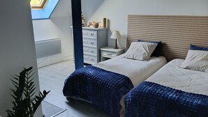 A bedroom with two beds, a skylight, a bedside table with a lamp, and a dresser.