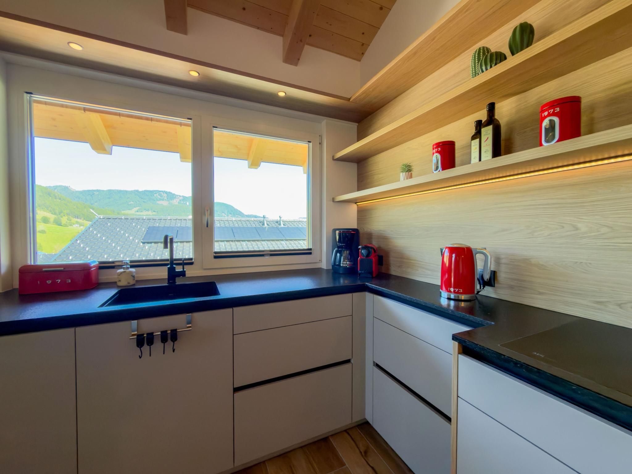 A modern kitchen with a large window, wooden shelves, and a view of solar panels.