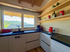 Een moderne keuken met een groot raam, houten planken en uitzicht op zonnepanelen.