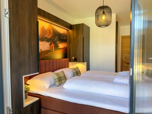 Ein Hotelzimmer mit Bett, einem Bild an der Wand, einer Hängelampe und einer Holztür.