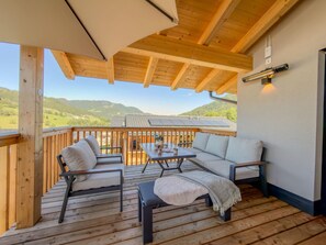Eine Holzterrasse mit Gartenmöbeln, einem Tisch und Blick auf eine Berglandschaft.
