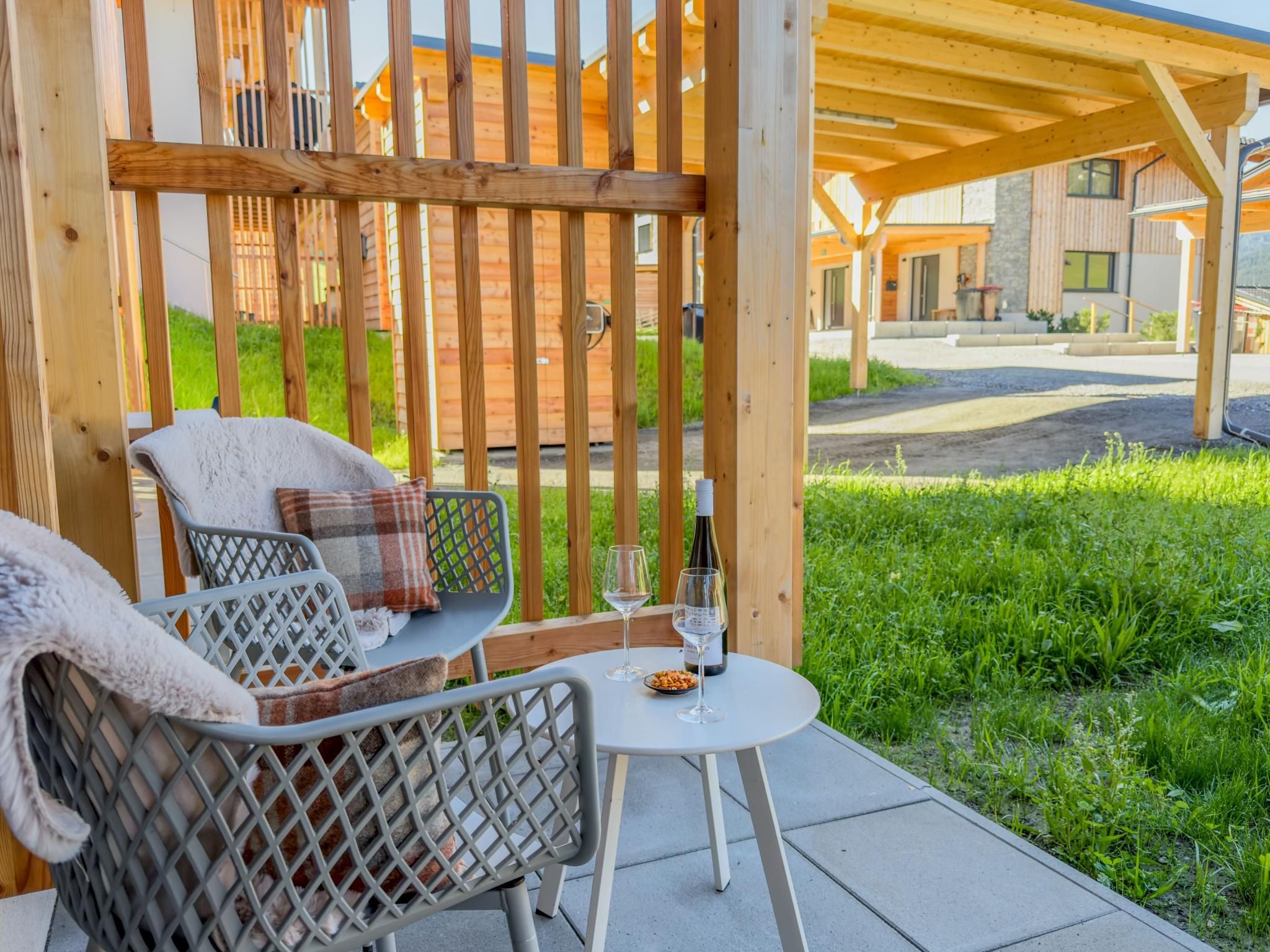 A covered outdoor seating area with a table, chairs, and a bottle of wine.
