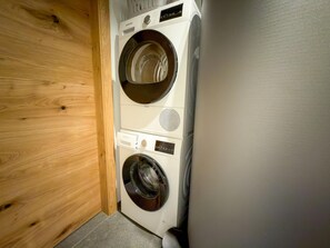 Eine Waschmaschine mit Frontöffnung und ein Trockner in einem Waschraum mit Holztür und Fliesenboden.