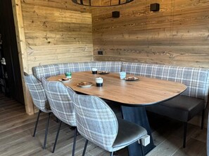 Ein runder Holztisch mit karierten Stühlen, umgeben von einer Holzwand mit eingebauten Lautsprechern.
