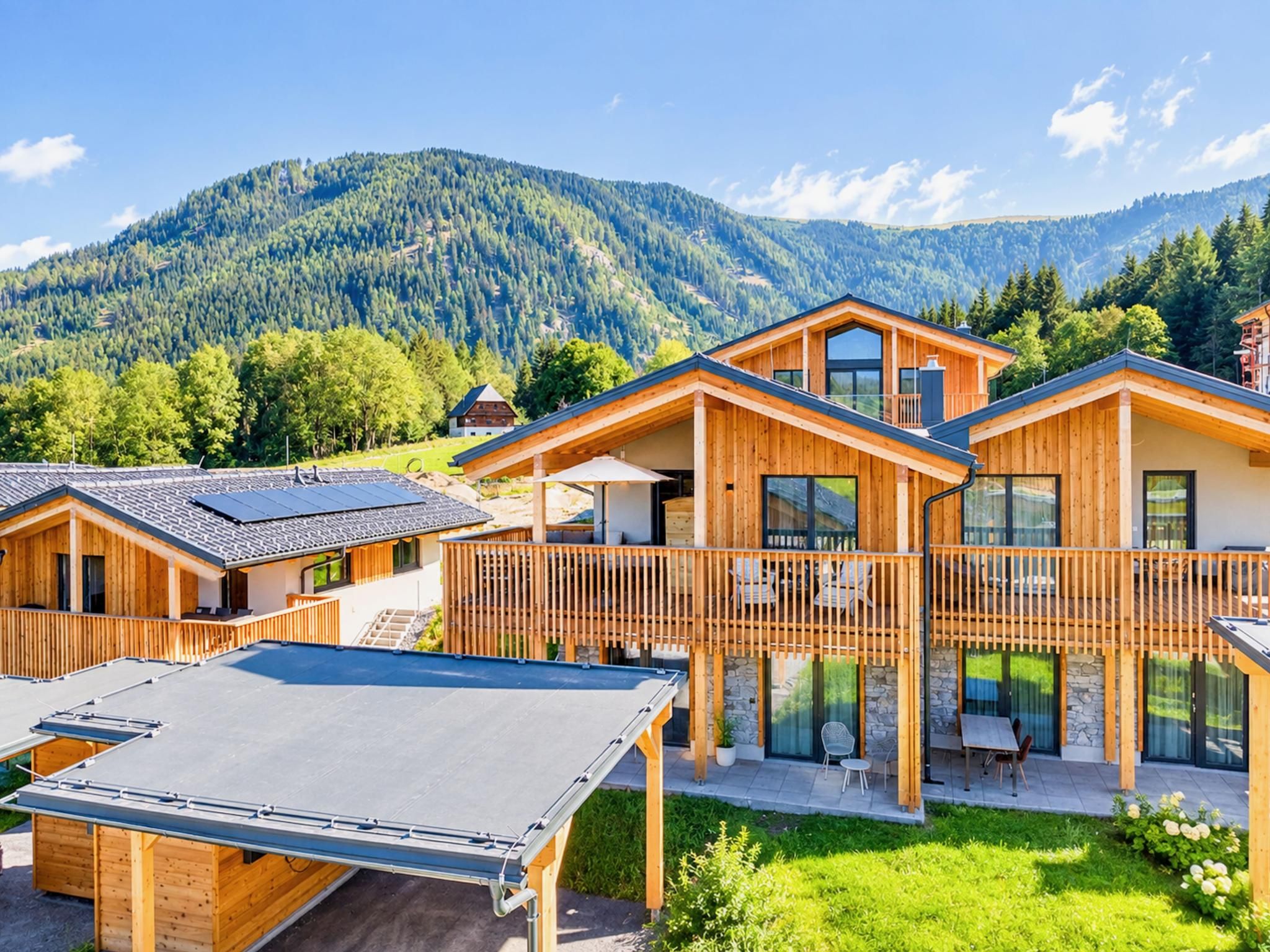 Eine moderne Holzlodge mit einer Terrasse und Sitzgelegenheit im Freien, vor einer Bergkulisse.