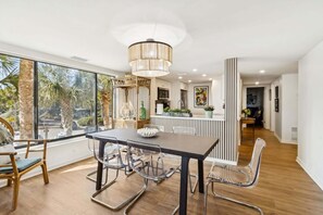 A modern kitchen with a dining area, large windows, and a view of palm trees. - Oceanfront | Private Balcony | Totally Renovated 2nd Floor Amelia Surf and Racquet Condo (Fernandina Beach)
