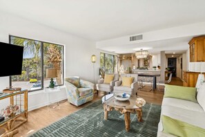 A spacious living room with a large window, a dining area, and a kitchen. - Oceanfront | Private Balcony | Totally Renovated 2nd Floor Amelia Surf and Racquet Condo (Fernandina Beach)