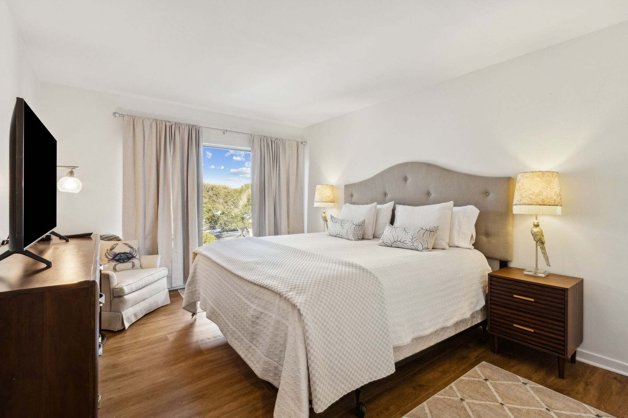 A bedroom with a bed, bedside tables, a TV, a sofa, and a window with curtains.
