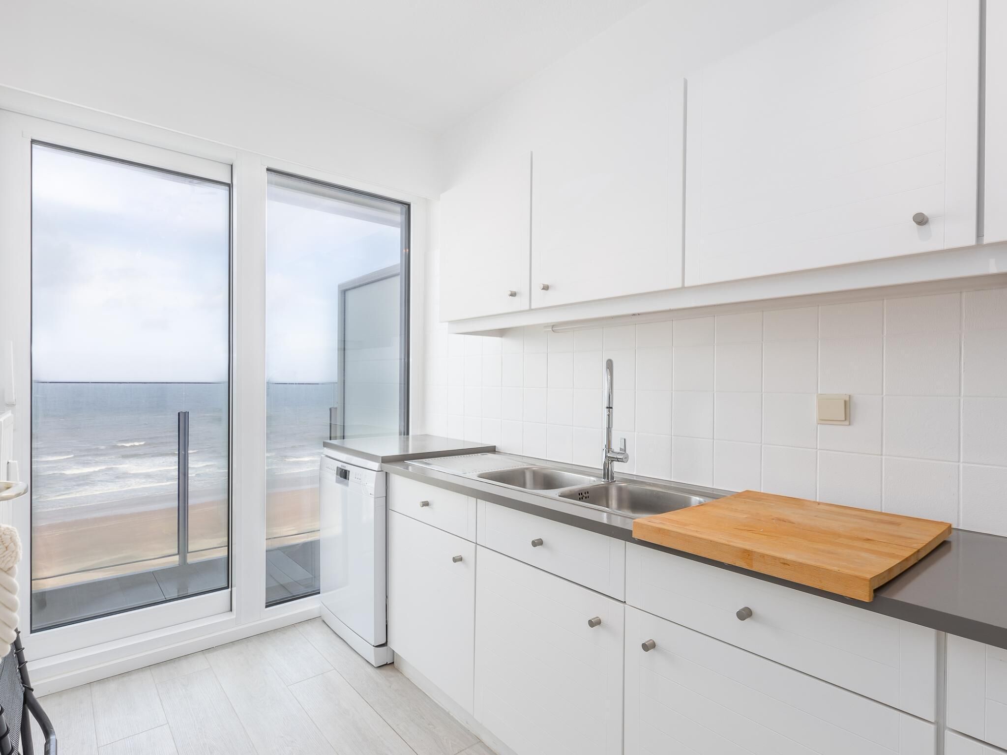 Una cucina moderna con mobili bianchi, un lavello in acciaio inossidabile e un piano di lavoro in legno.