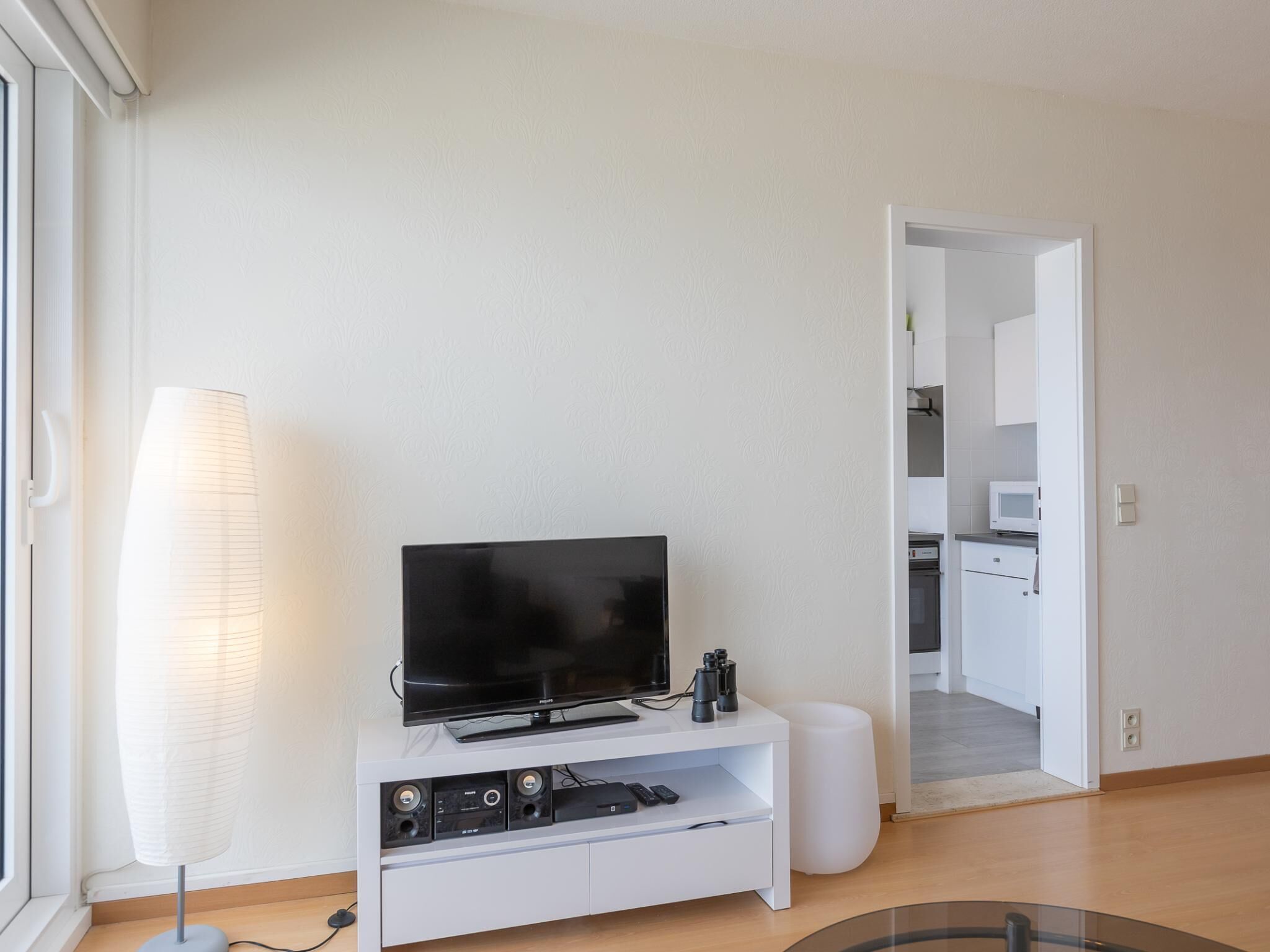 A modern living room with a flat-screen TV on a white entertainment unit, a floor lamp, and a white ottoman.