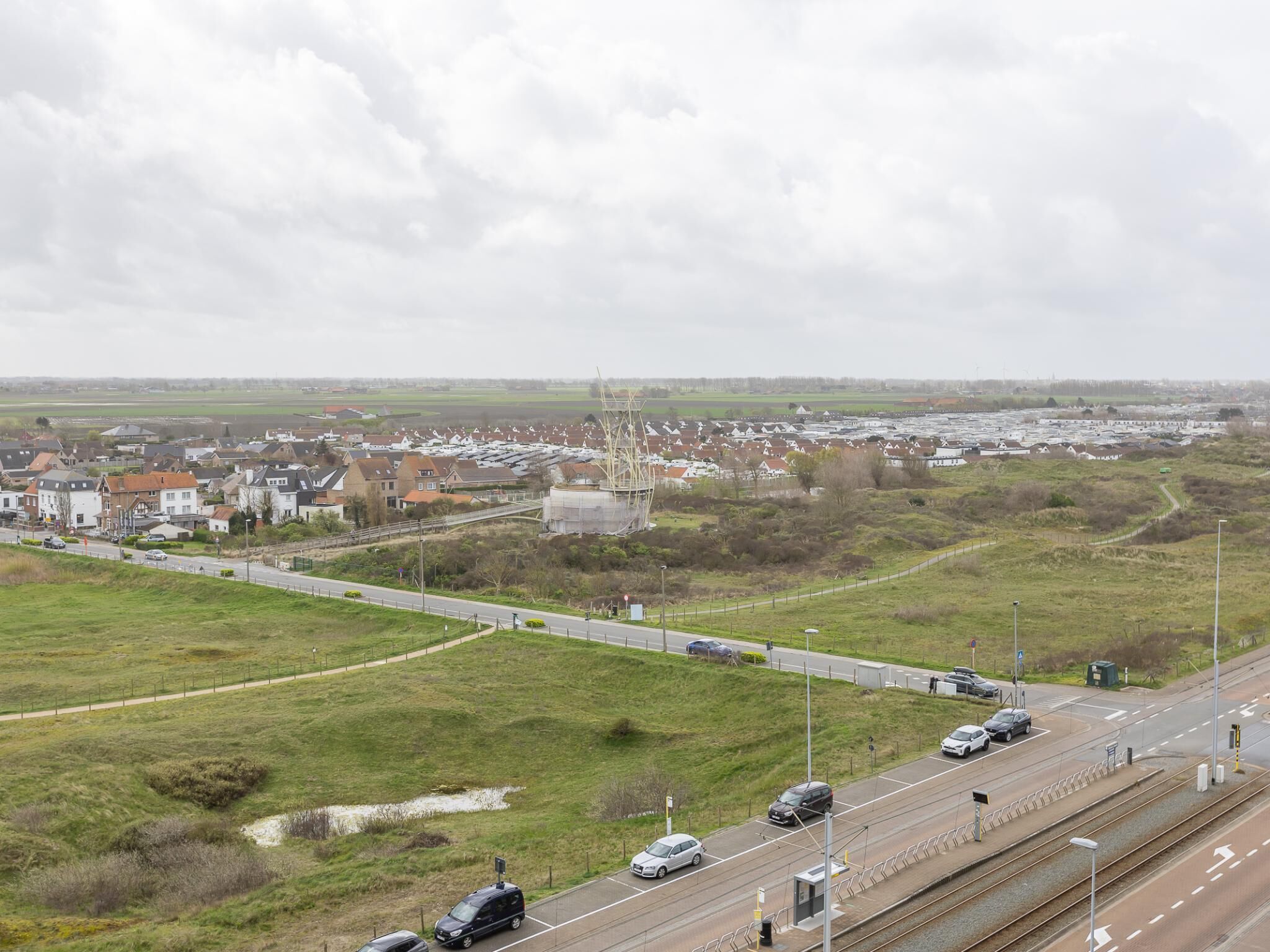 A highway with multiple lanes, a railway track, and a residential area with houses and a large industrial structure.