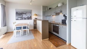 A modern kitchen with a built-in oven, a refrigerator, and a dining area with a table and chairs. - Apartment on the 8th floor with terrace (Middelkerke)