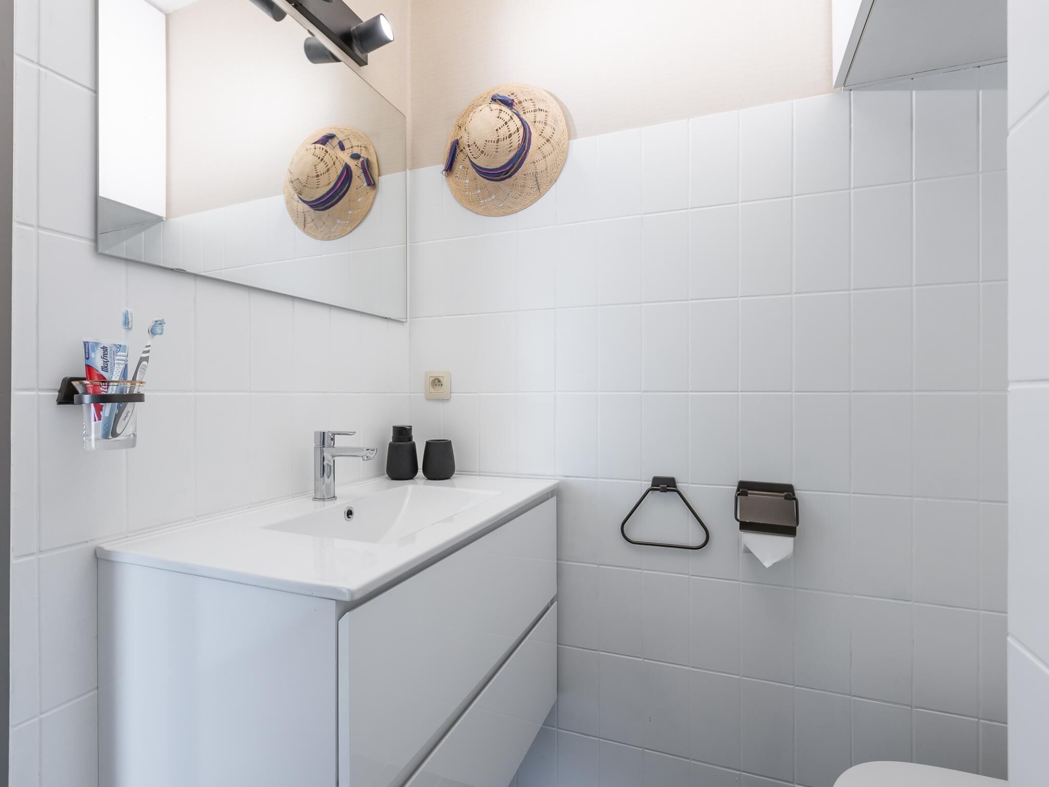 Un baño moderno con un lavamanos blanco, un espejo y dos sombreros en la pared.