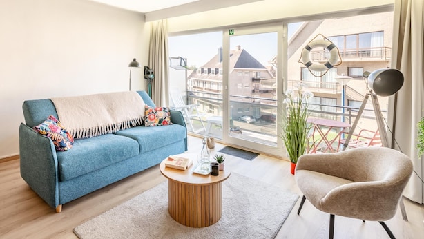 Una sala de estar moderna con un sofá azul, una mesa de centro redonda de madera, un sillón beige y un telescopio.