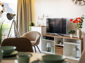 Ein modernes Wohnzimmer mit Fernseher, Stativ, Stuhl und Blumentopf.