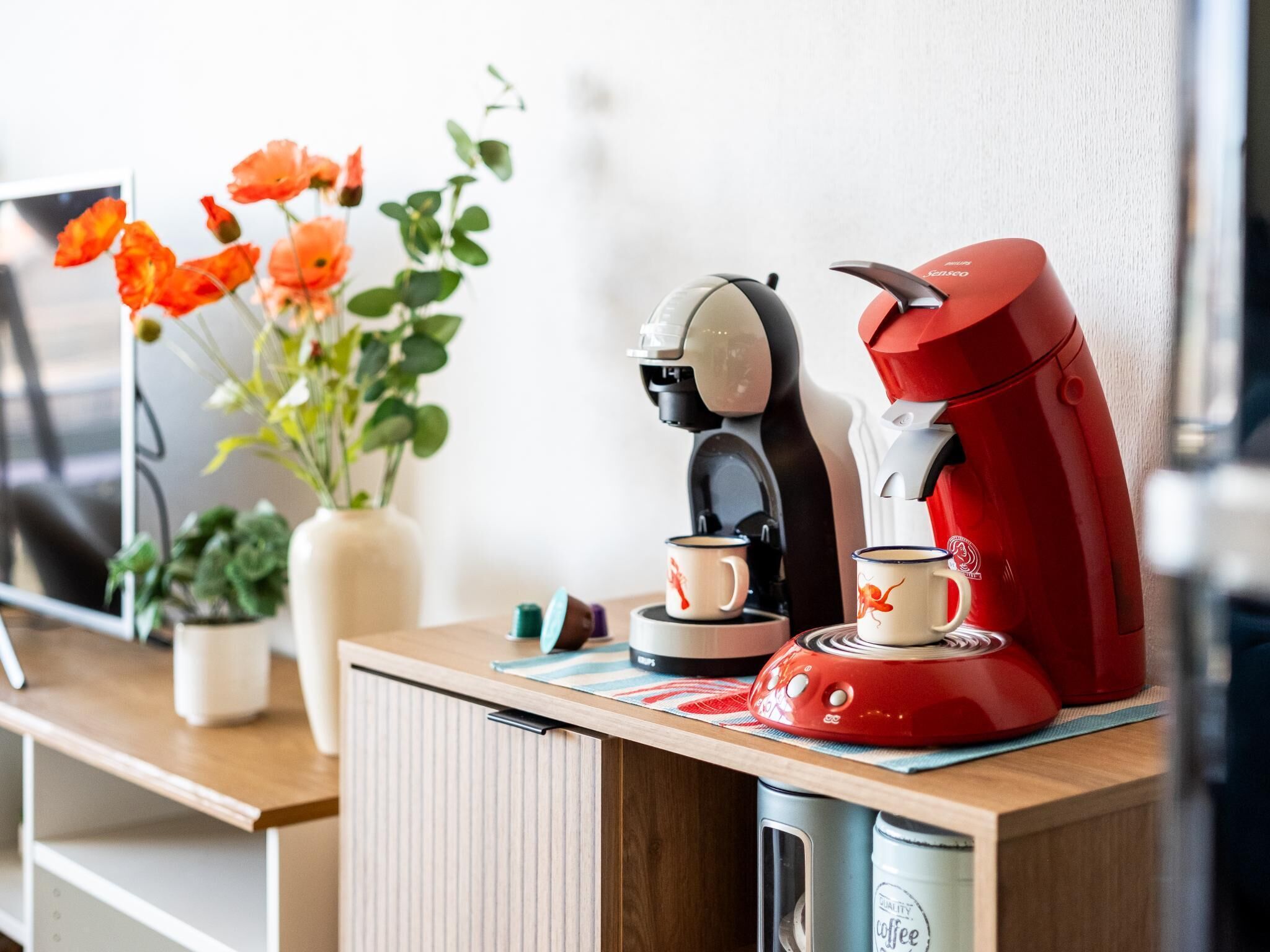 A kitchenette with a coffee maker, a red coffee pot, and a cup on the counter.