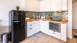 Cocina moderna con armarios blancos, refrigerador negro, encimera de madera y salpicadero con azulejos verdes.