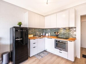 Eine moderne Küche mit weißen Schränken, einem schwarzen Kühlschrank, einer Holz Arbeitsplatte und einer grüngesteuerten Spritzschutzwand.