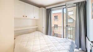 A bedroom with a bed, white wardrobe, and a balcony with curtains. - centrally located apartment by the beach (Koksijde)
