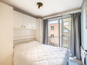 A bedroom with a bed, white wardrobe, and a balcony with curtains. - centrally located apartment by the beach (Koksijde)