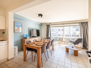 A modern apartment with a dining area, kitchenette, and a large window with a city view. - centrally located apartment by the beach (Koksijde)