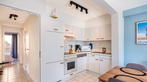 A modern kitchen with white cabinets, a microwave, stove, and a dining area with a wooden table and chairs. - centrally located apartment by the beach (Koksijde)